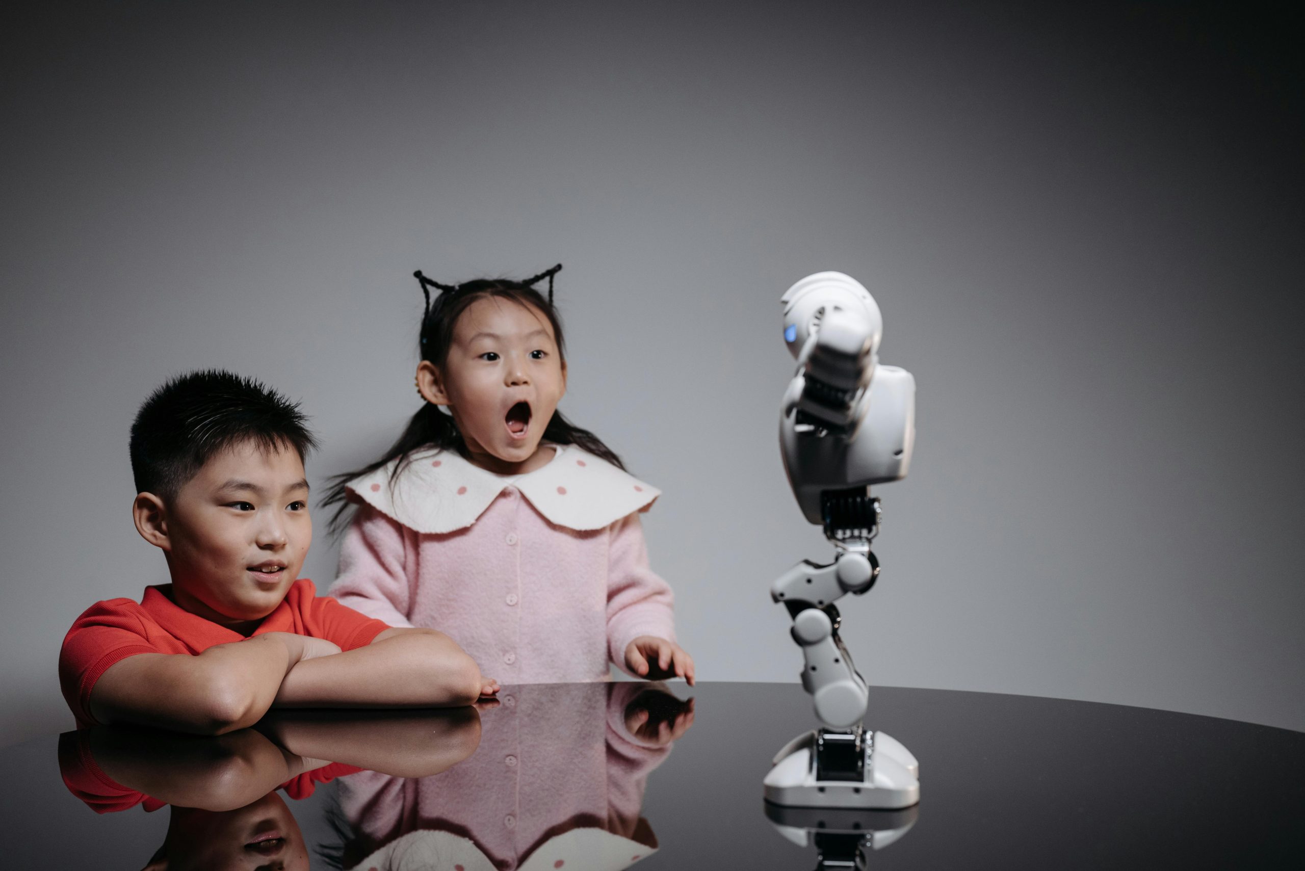 Two children fascinated by a toy robot, showcasing excitement and curiosity indoors.